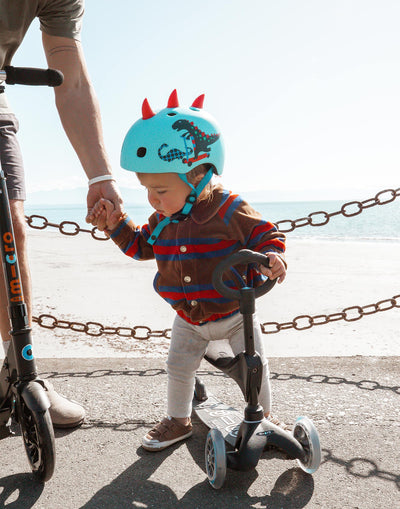 toddler riding his 3 wheel black eco scooter at the beach with mini seat attachment