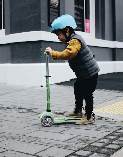 boy riding a green mini deluxe 3 wheel toddler scooter through town