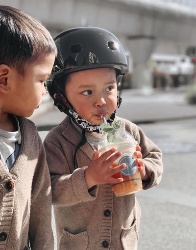 toddler wearing black scooter and bike helmet while sipping on a juice