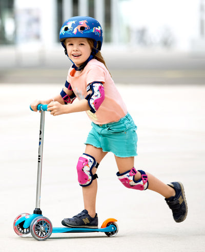 toddler wearing unicorn knee and elbow pads while riding mini scooter