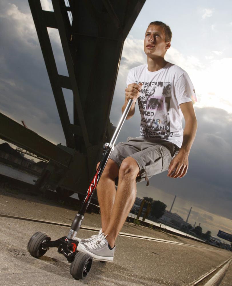 adult riding their volcano grey kickboard 3 wheel adult scooter across a bridge